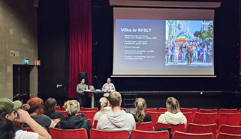 Två personer föreläser, publik i förgrunden. 