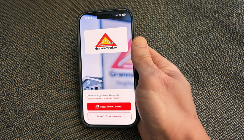 Närbild av hand som håller i mobiltelefon. Text på skärmen: Grannsamverkan.