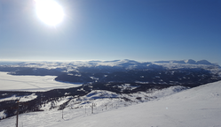 Vy över fjäll och sjö. Solen skiner, snö på marken.