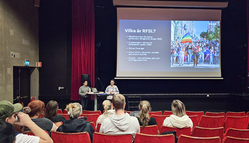 Två personer föreläser, publik i förgrunden. 