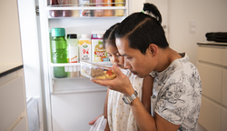 Pappa och dotter luktar på mat från kylskåp.